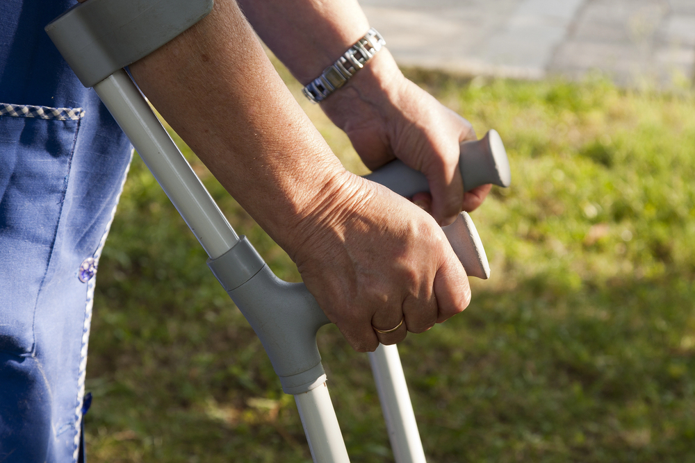 Close-up of an adult’s hands gripping gray forearm crutches outdoors, with grass in the background, suggesting mobility support during recovery or injury.